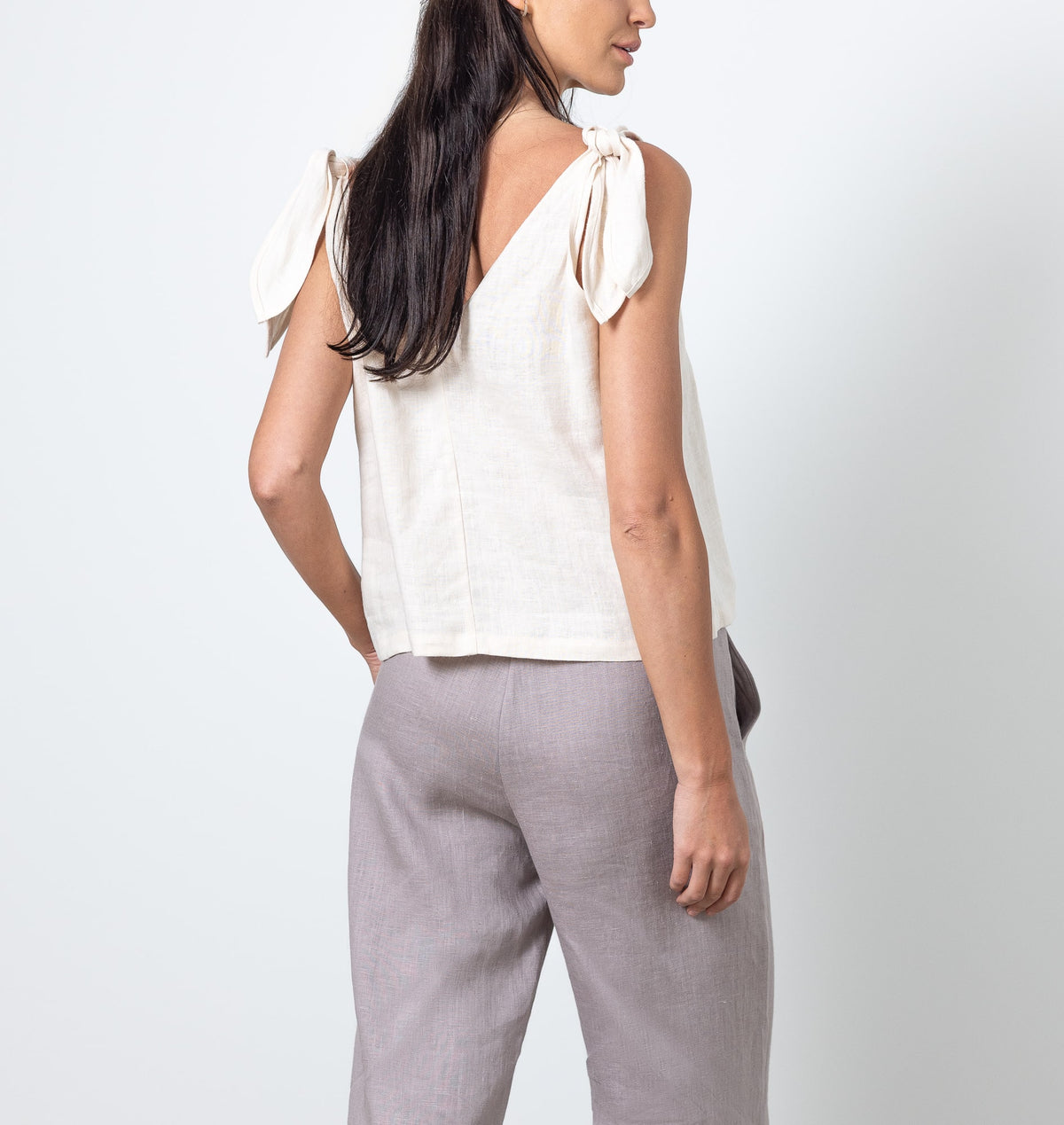 Close-up of woman wearing V-neck white linen top with shoulder bows, minimal natural look.
