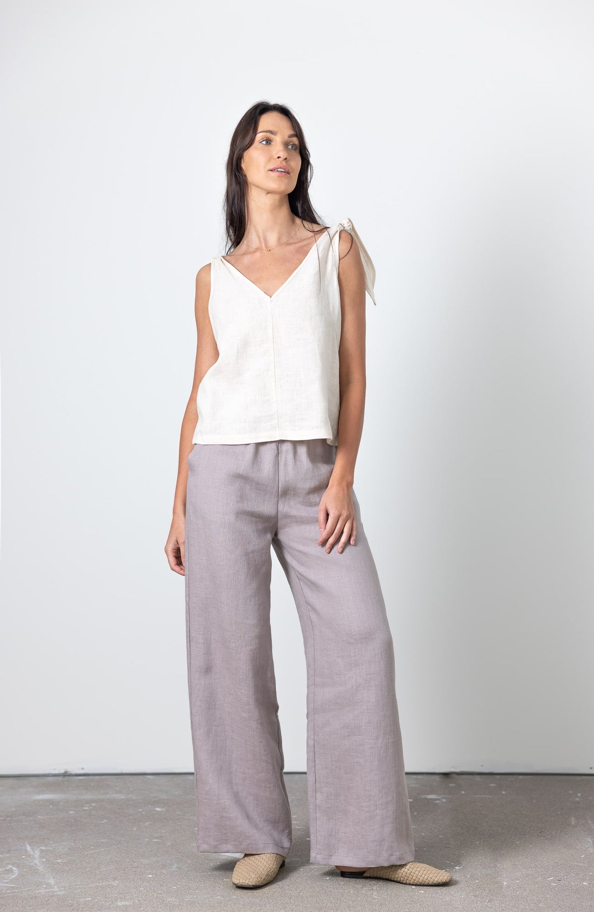 Front view of woman in white linen crop top with bow straps, styled with light grey loose-fit linen pants.