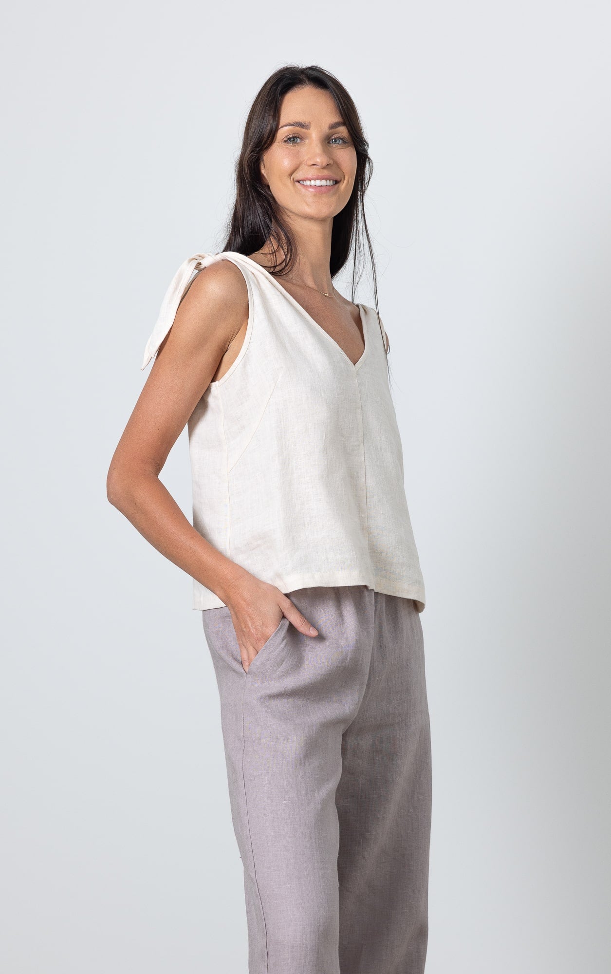 Woman wearing white linen crop top with bow tie shoulders and light grey wide leg linen pants, back view.