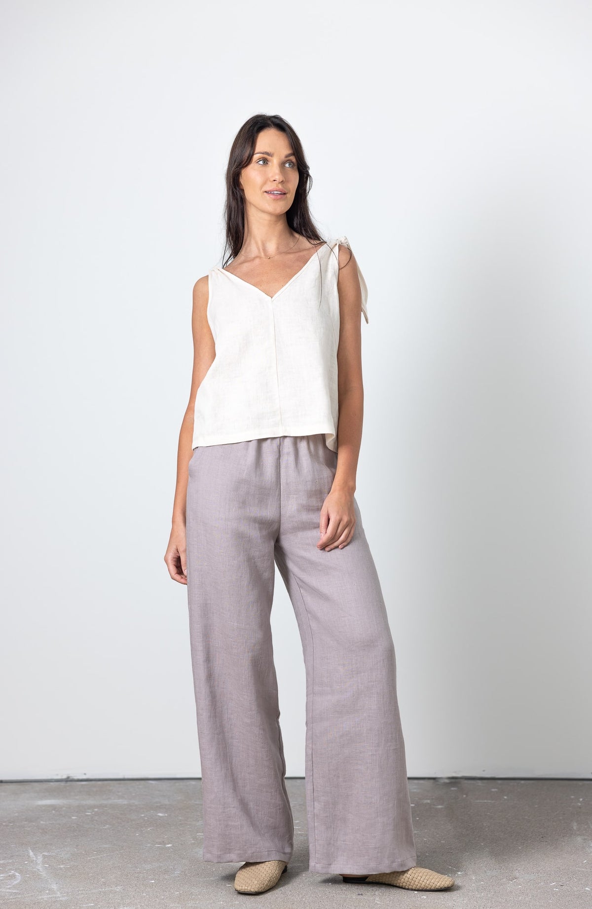 Full body shot of woman wearing bow shoulder white linen top and wide leg linen trousers