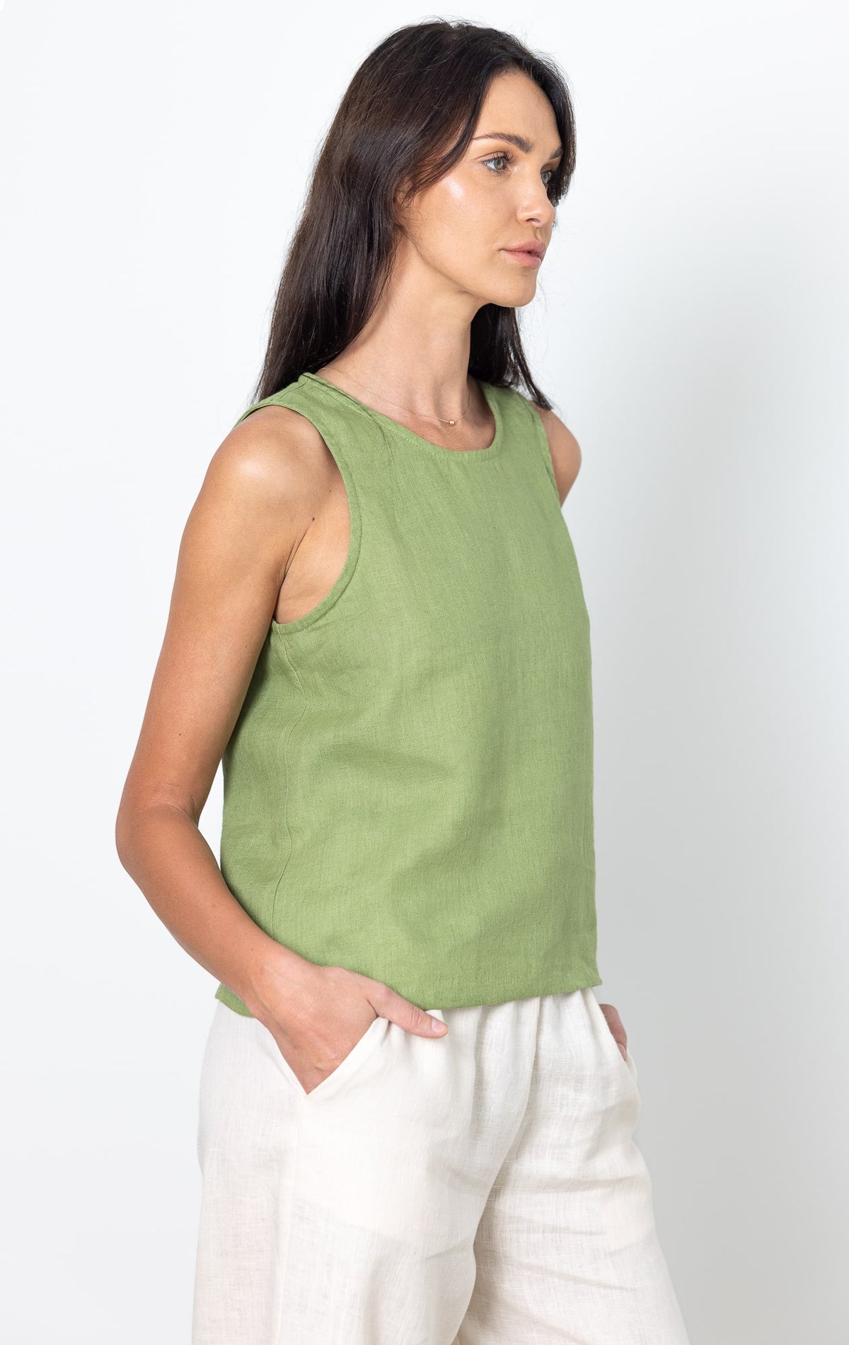 Woman wearing a green sleeveless LINEN top and white pants against a white background