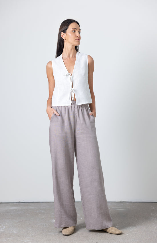 Full-body shot of a woman in a sleeveless linen tie front top and high-waisted wide leg linen pants, sustainable summer look