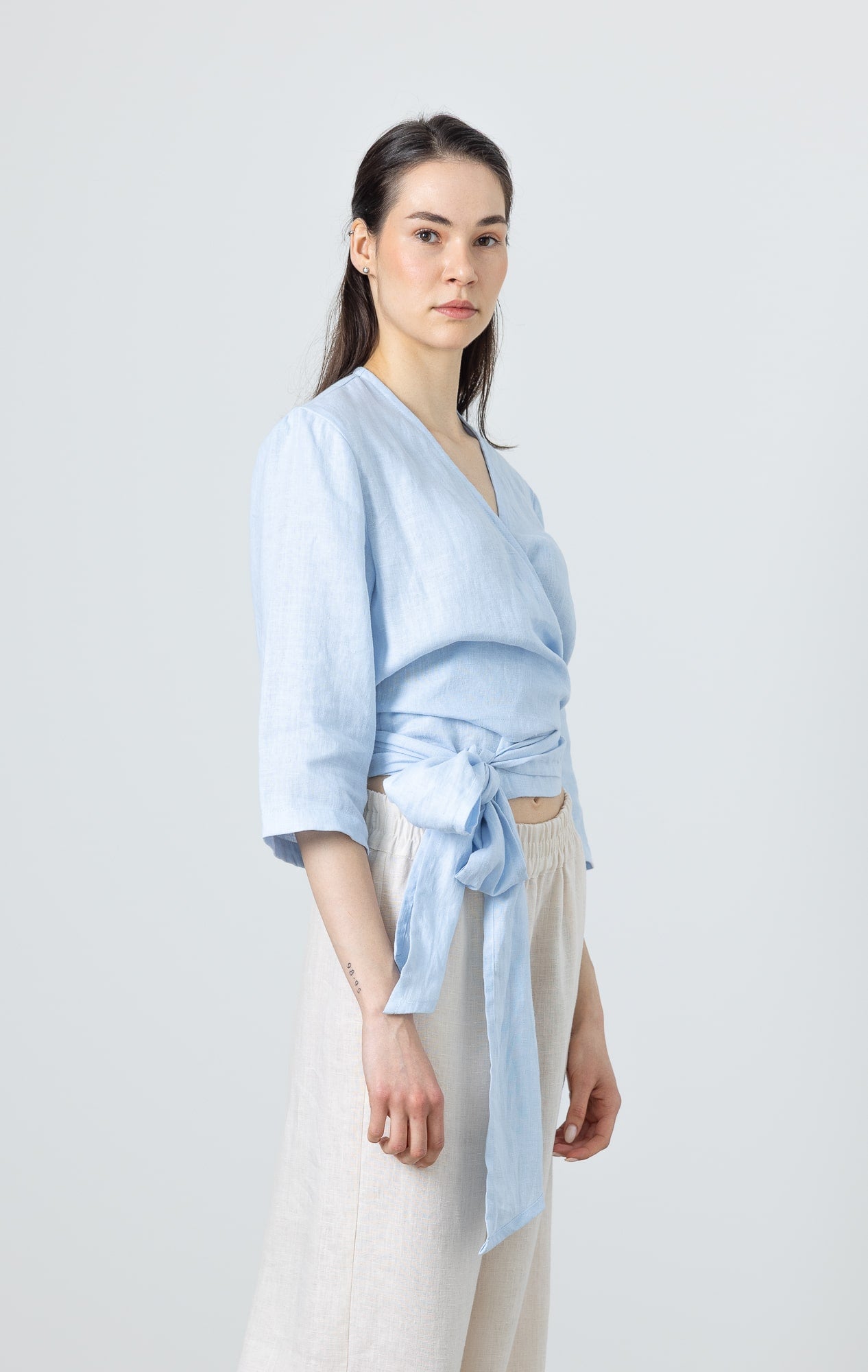 Side view of a woman in a soft blue linen wrap blouse – minimalist linen fashion for women