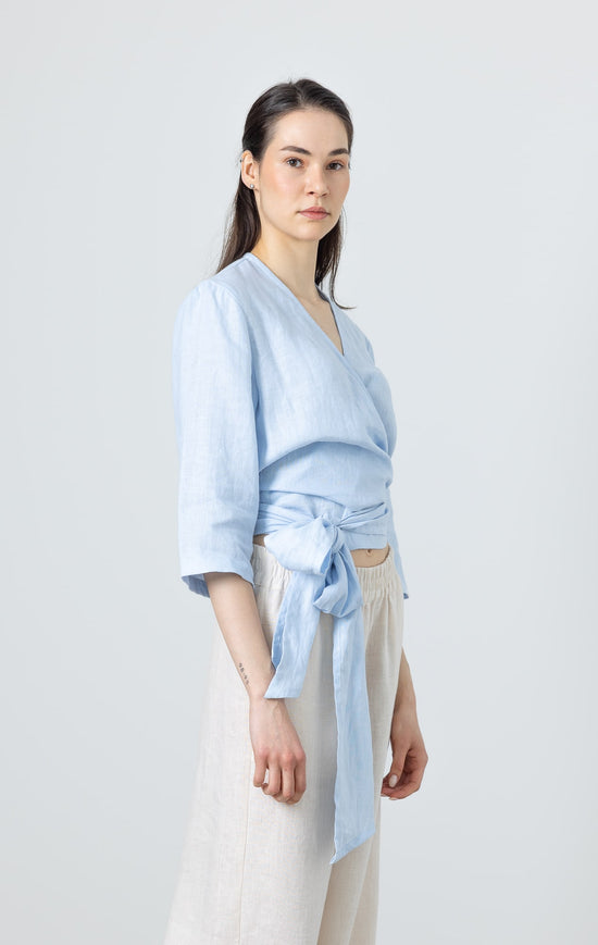 Side view of a woman in a soft blue linen wrap blouse – minimalist linen fashion for women