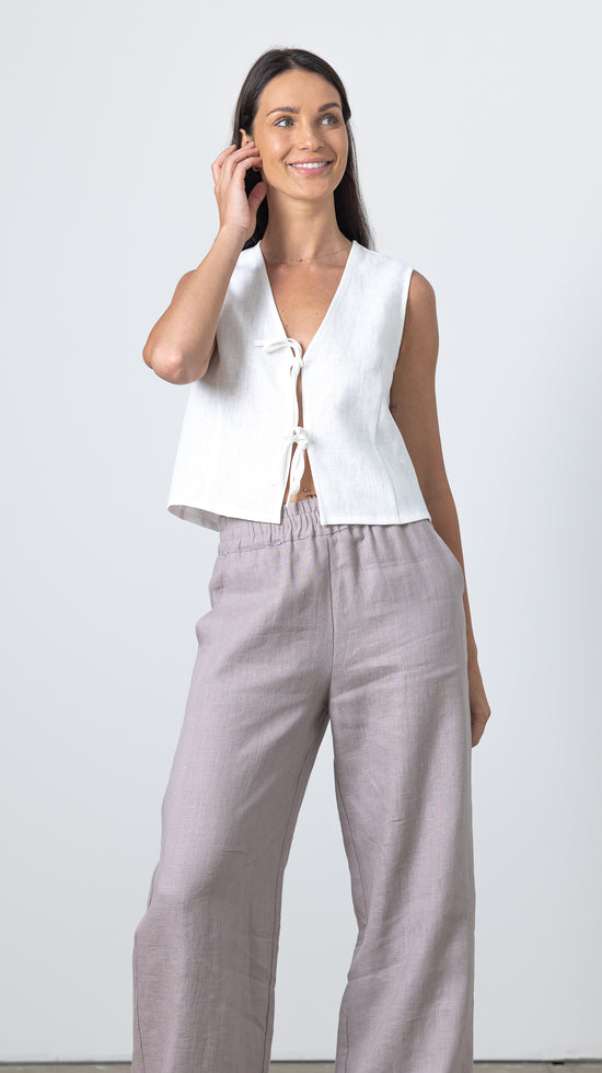 Woman touching her hair while wearing a white linen tie front top and relaxed linen trousers, minimalist linen fashion