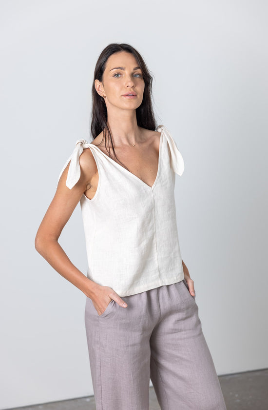 Side view of smiling woman in a sleeveless white linen top with tied straps and relaxed grey linen pants