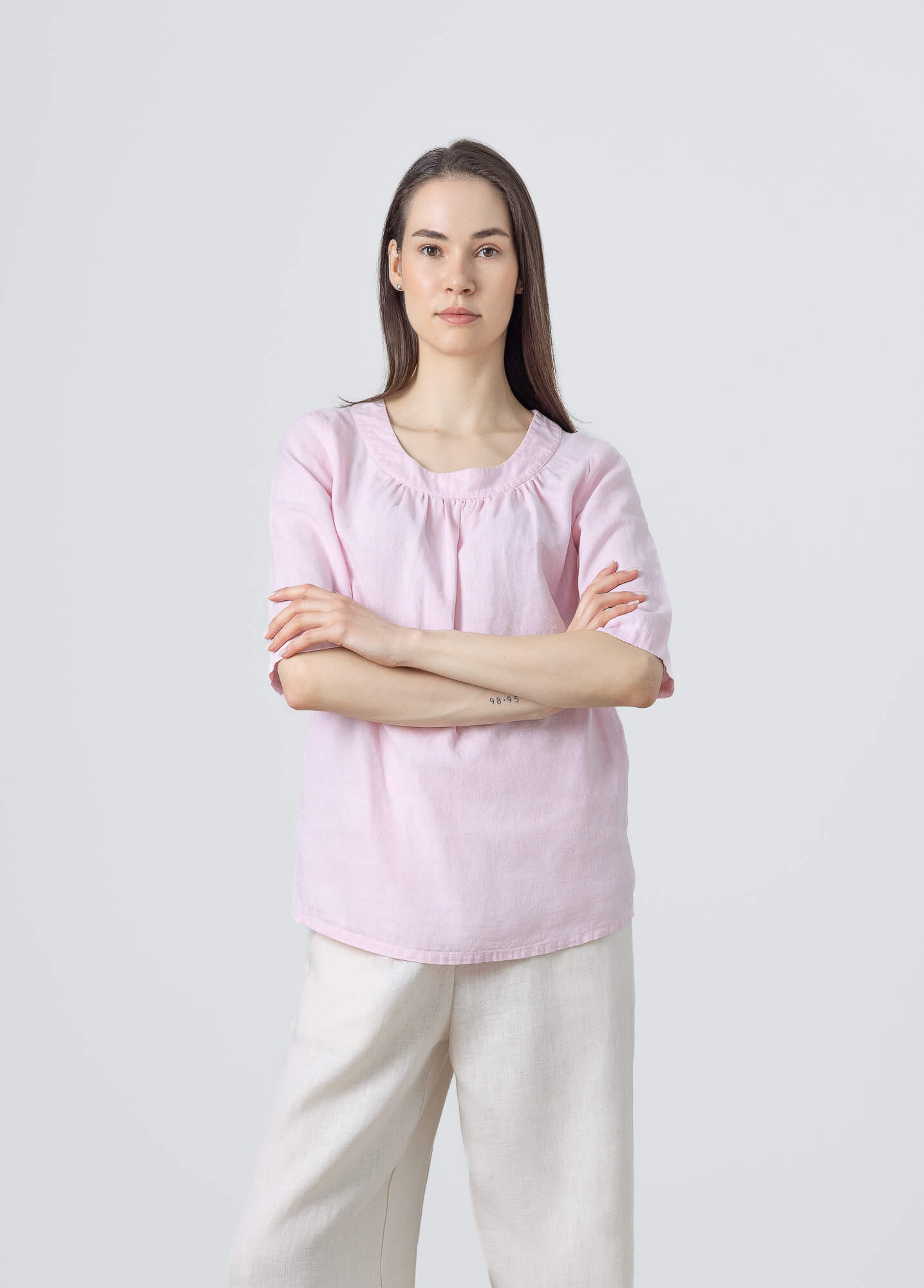 Women's blush pink linen blouse with a gathered round neckline and half sleeves.