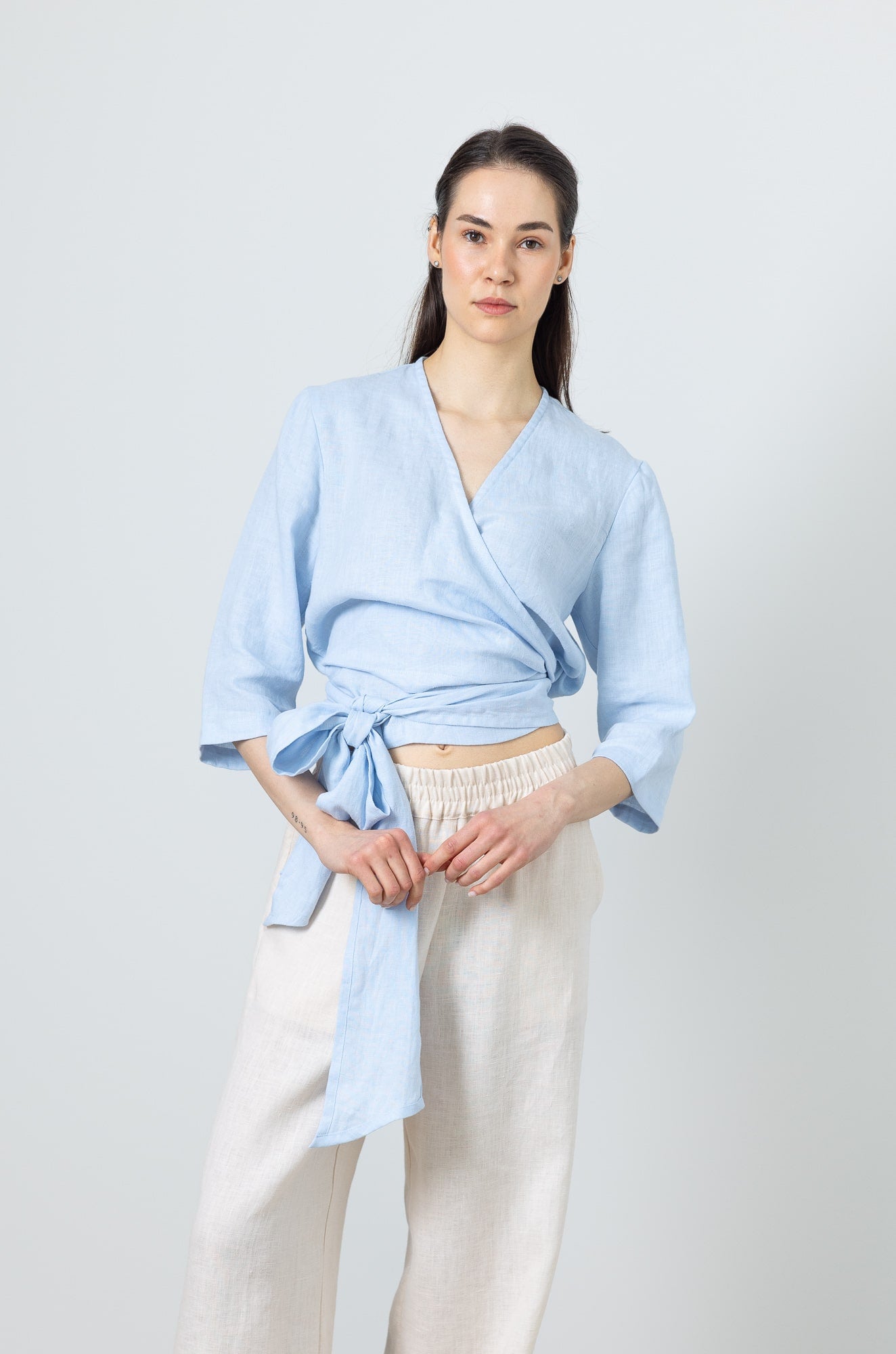 Woman wearing a blue linen wrap top with long waist tie – breathable summer blouse for women
