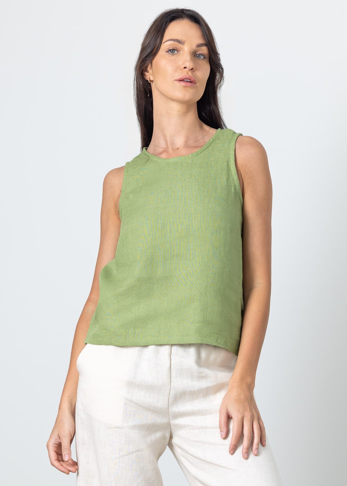 Woman wearing a green linen crop top  and white linen pants against a light gray background