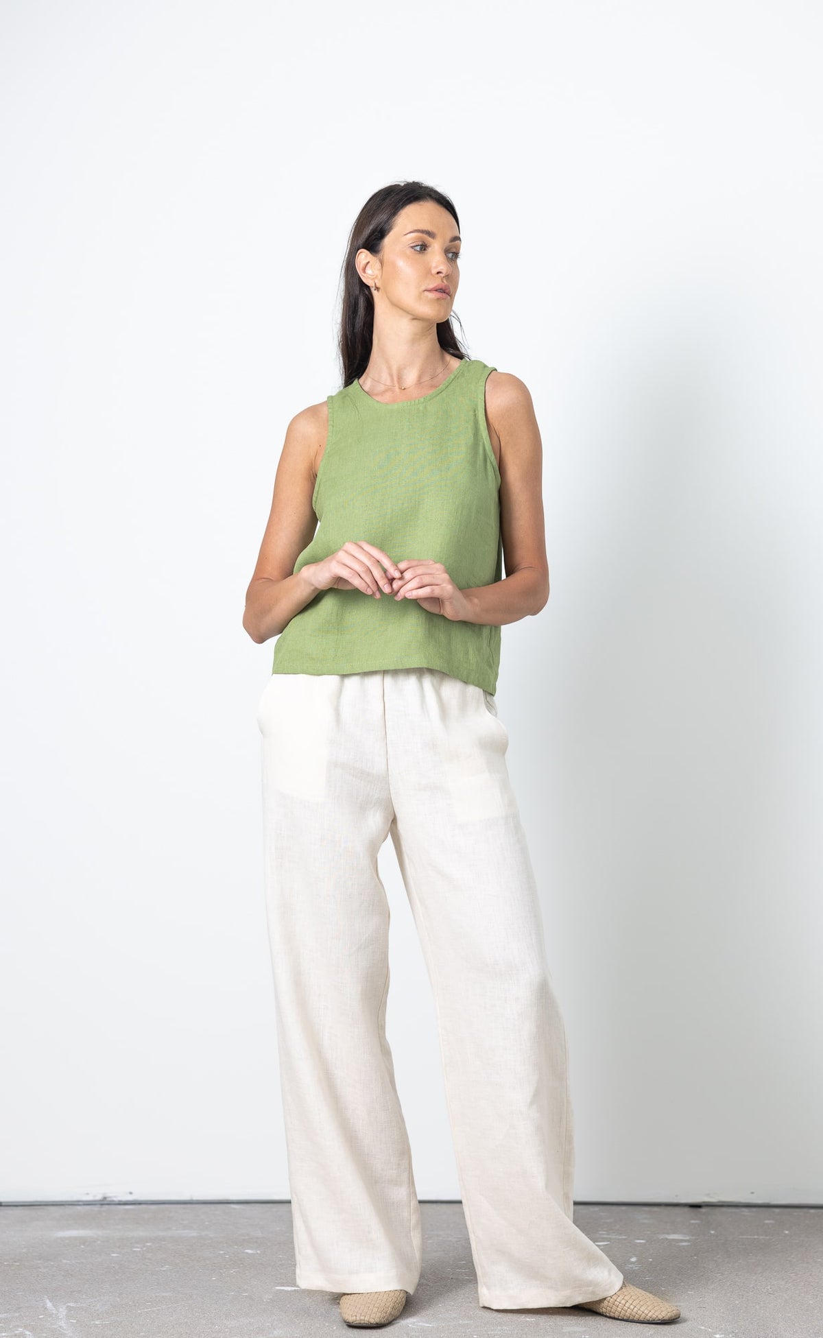 Woman wearing a sleeveless linen top and white linen trousers against a white background